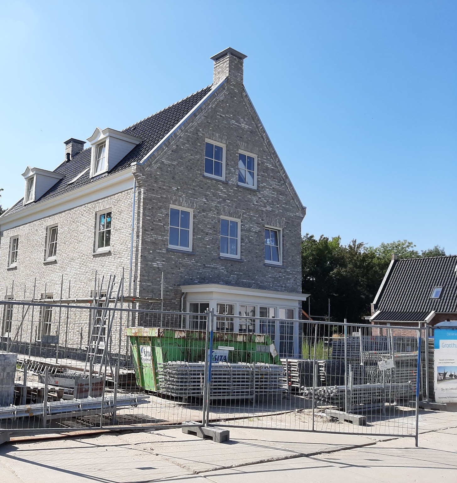 Grijze bakstenen nieuwbouwwoning achter bouwhekken