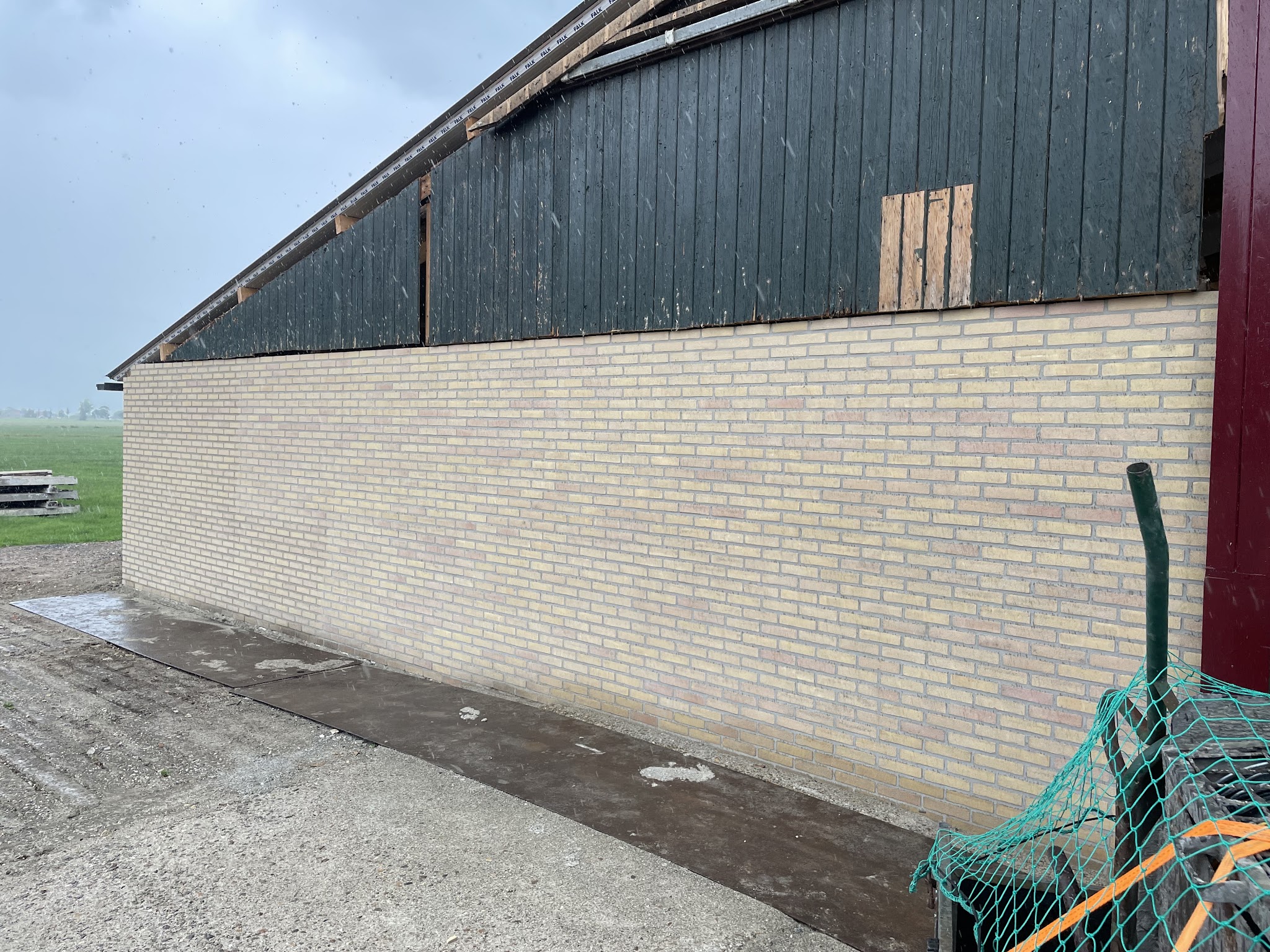 Lange gele bakstenen muur onder een donkere houten schuurgevel