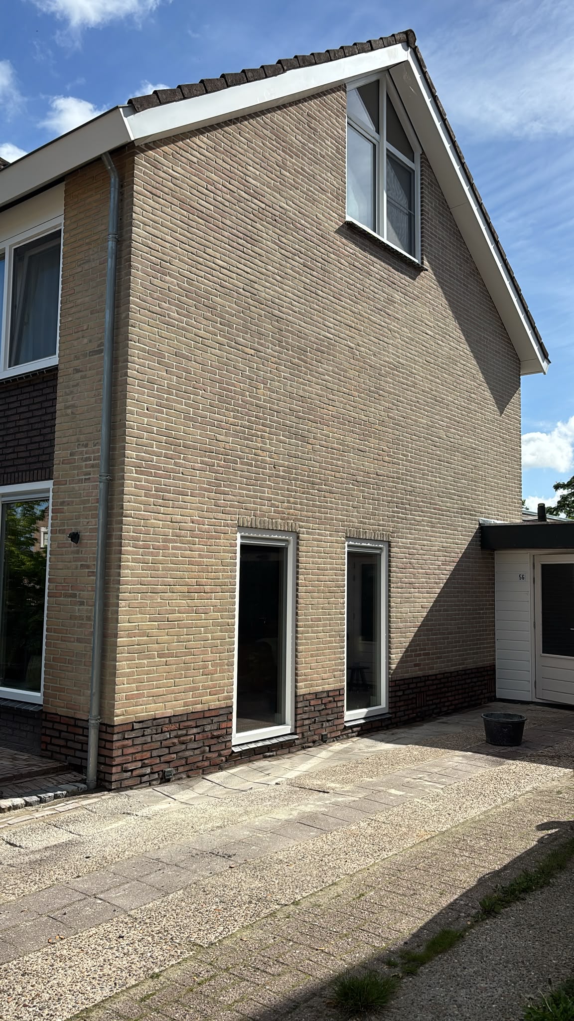 Gele bakstenen kopgevel met donkere plint onder een blauwe lucht