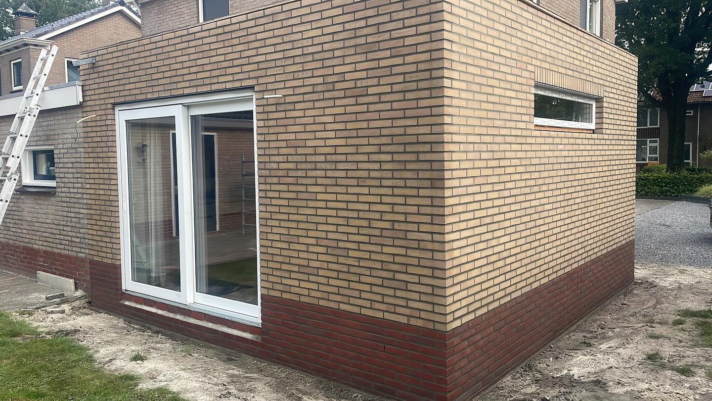 Aanbouw van gele baksteen met een rode plint en openslaande deuren