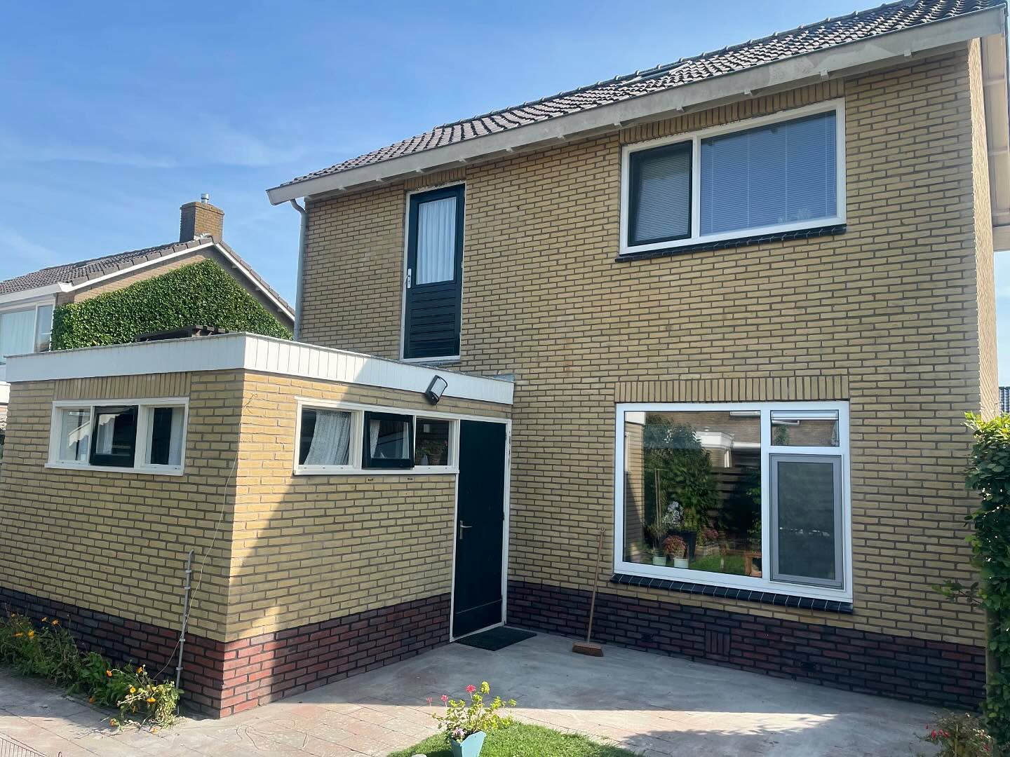 Woning van gele baksteen met een lage aanbouw en een donkere plint